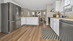 A modern kitchen with stainless steel appliances, white cabinetry, and a central island. - Luxurious Grand Park Family Home with Fenced Yard and Game Room! (Westfield)