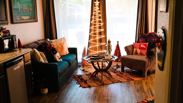 Un salon chaleureux avec un canapé, un fauteuil et une table basse. Un sapin de Noël décoré, illuminé, se trouve au centre de la pièce.