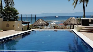 Une piscine avec des chaises longues, des palmiers et une vue sur l’océan.