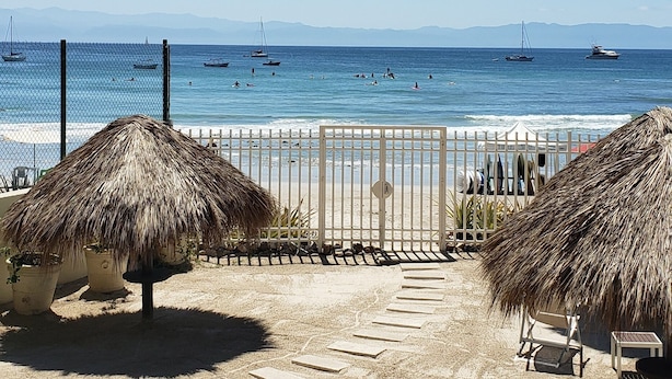 Une vue sur la plage avec un parasol en chaume, une table et des chaises.