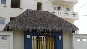 Un bâtiment dont l’entrée est surmontée d’un toit de chaume et porte l’inscription « El Farito », avec une porte bleue, un portail jaune et des plantes en pot.