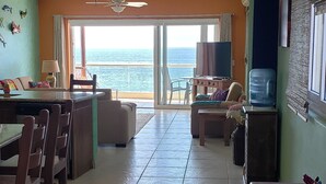 Un vaste espace de vie avec un balcon donnant sur la mer, aménagé avec une table à manger, des chaises et un canapé.