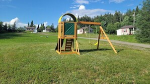 A playground with a swing set and a climbing structure in a grassy field with houses in the background. - 02) Northwoods Cabin (Stewartstown)