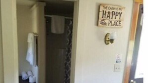 A hotel room with a door leading to a bathroom. A sign on the door reads "The cabin is my happy place." - 02) Northwoods Cabin (Stewartstown)