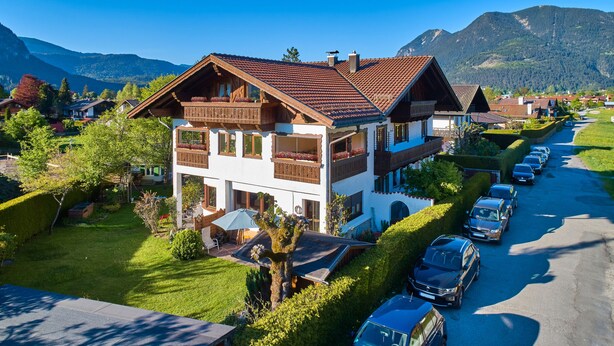 Eine zweistöckige Chalet mit geneigtem Dach, Holzbalkonen und einem Garten.