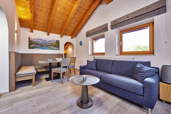 Un salon moderne avec un plafond en bois, un canapé bleu, une table ronde et un coin repas avec des chaises.