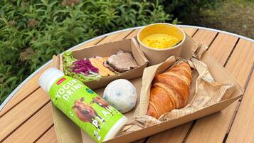 A meal with a yogurt drink, a croissant, and a salad on a wooden table outdoors.