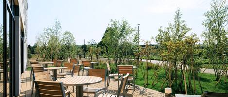 An outdoor patio area with multiple tables and chairs, surrounded by greenery and trees.