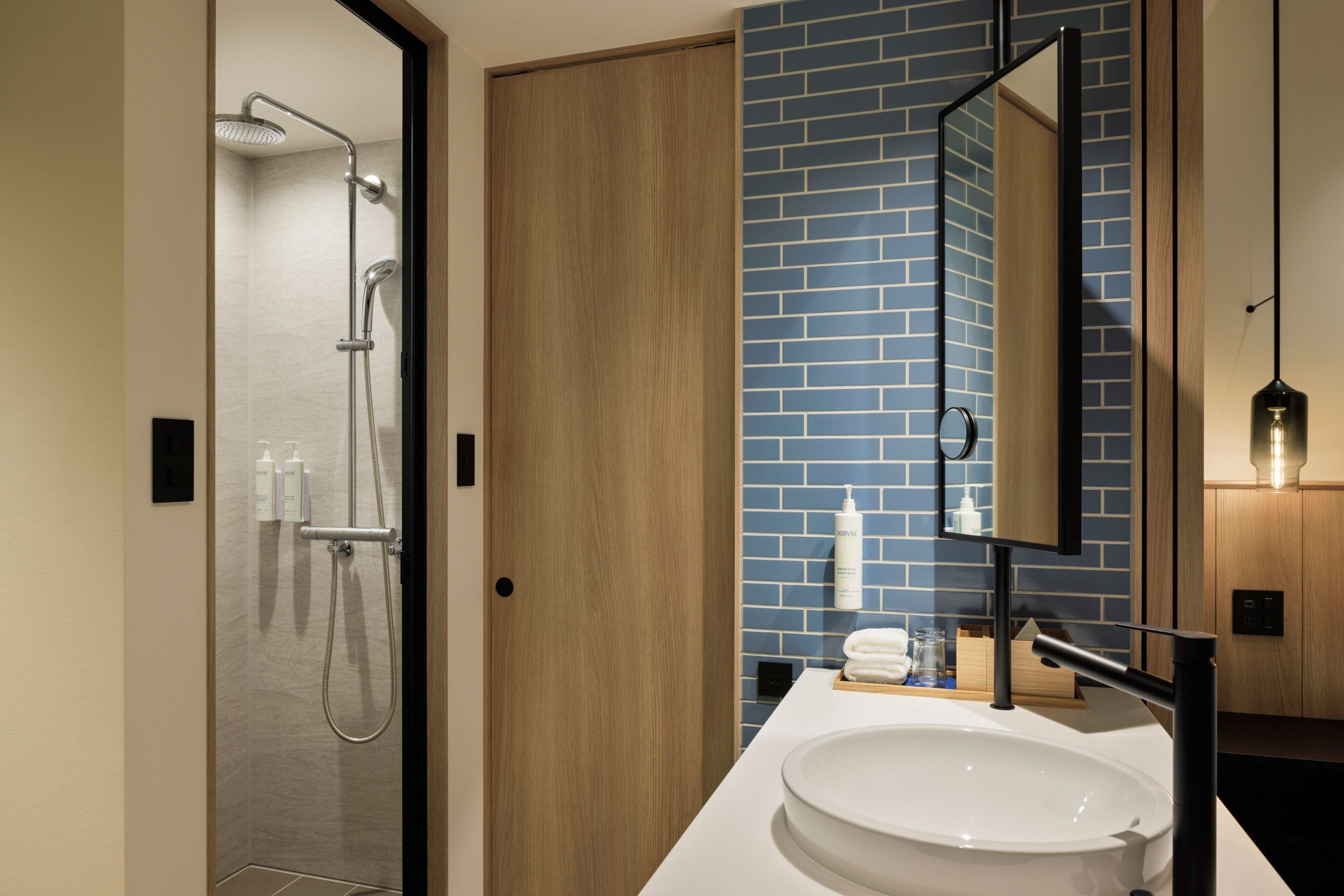 Un baño moderno con cabina de ducha de vidrio, puerta de madera, lavamanos blanco y pared con azulejos azules.