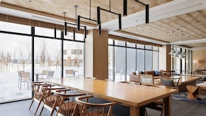 Un comedor moderno con una larga mesa de madera y sillas, ventanas amplias y luminarias contemporáneas.