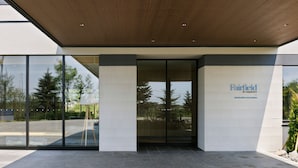 Een modern gebouw met een entree, glazen deuren, een houten plafond en een bordje met de tekst 