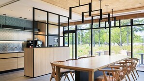 Een moderne keuken met een lange eettafel en stoelen, grote ramen en uitzicht op het buiten.