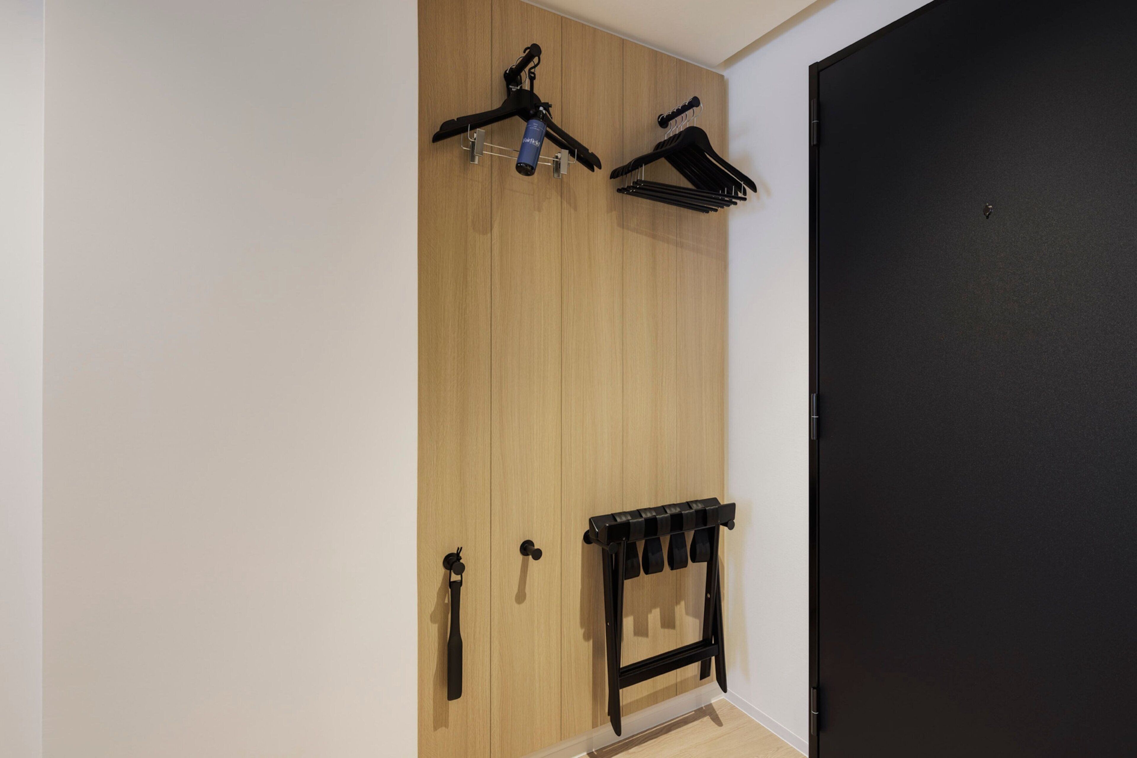 A room with a wooden wardrobe, a black door, and a black coat rack with hooks.