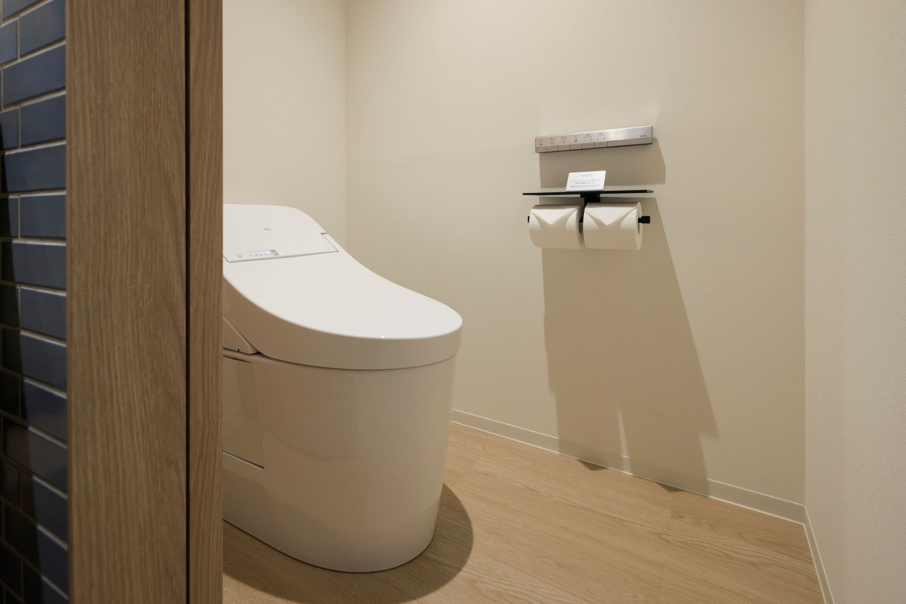 A modern bathroom with a white toilet, a small shelf with a tissue box, and a wooden floor.