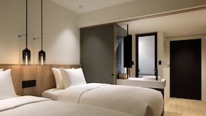 Een moderne hotelkamer met twee bedden, een houten hoofdbord, een grote spiegel en een badkamer met wastafel en spiegel.