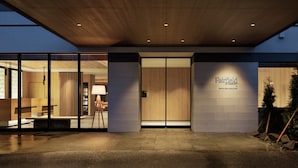 Een moderne hotelentree met een houten plafond, glazen deuren en een bord met de tekst 'Fairfield by Marriott'.