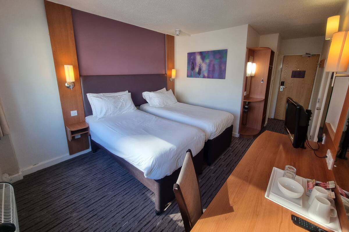 Une chambre d’hôtel avec deux lits, un bureau en bois avec un plateau, une télévision et un tableau au mur.