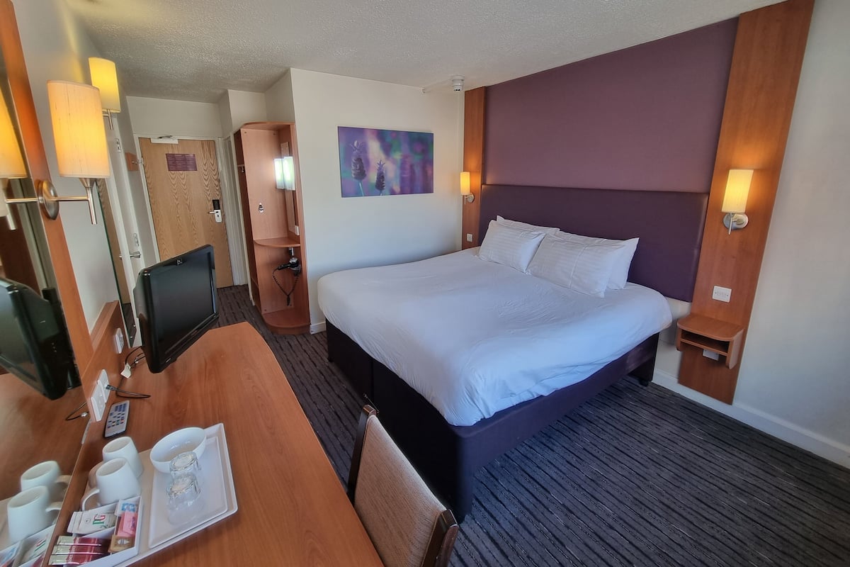 Une chambre d'hôtel avec un grand lit, un bureau sur lequel se trouve un plateau avec des articles pour le petit-déjeuner, une télévision et une armoire en bois.