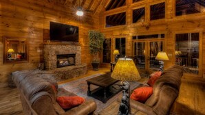 Un intérieur chaleureux de chalet en bois, avec une cheminée en pierre, des canapés en cuir et un grand téléviseur.