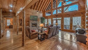 L’intérieur de cette vaste cabane en rondins est agrémenté d’une cheminée, de sièges confortables et de grandes fenêtres qui offrent une vue imprenable sur la forêt environnante.