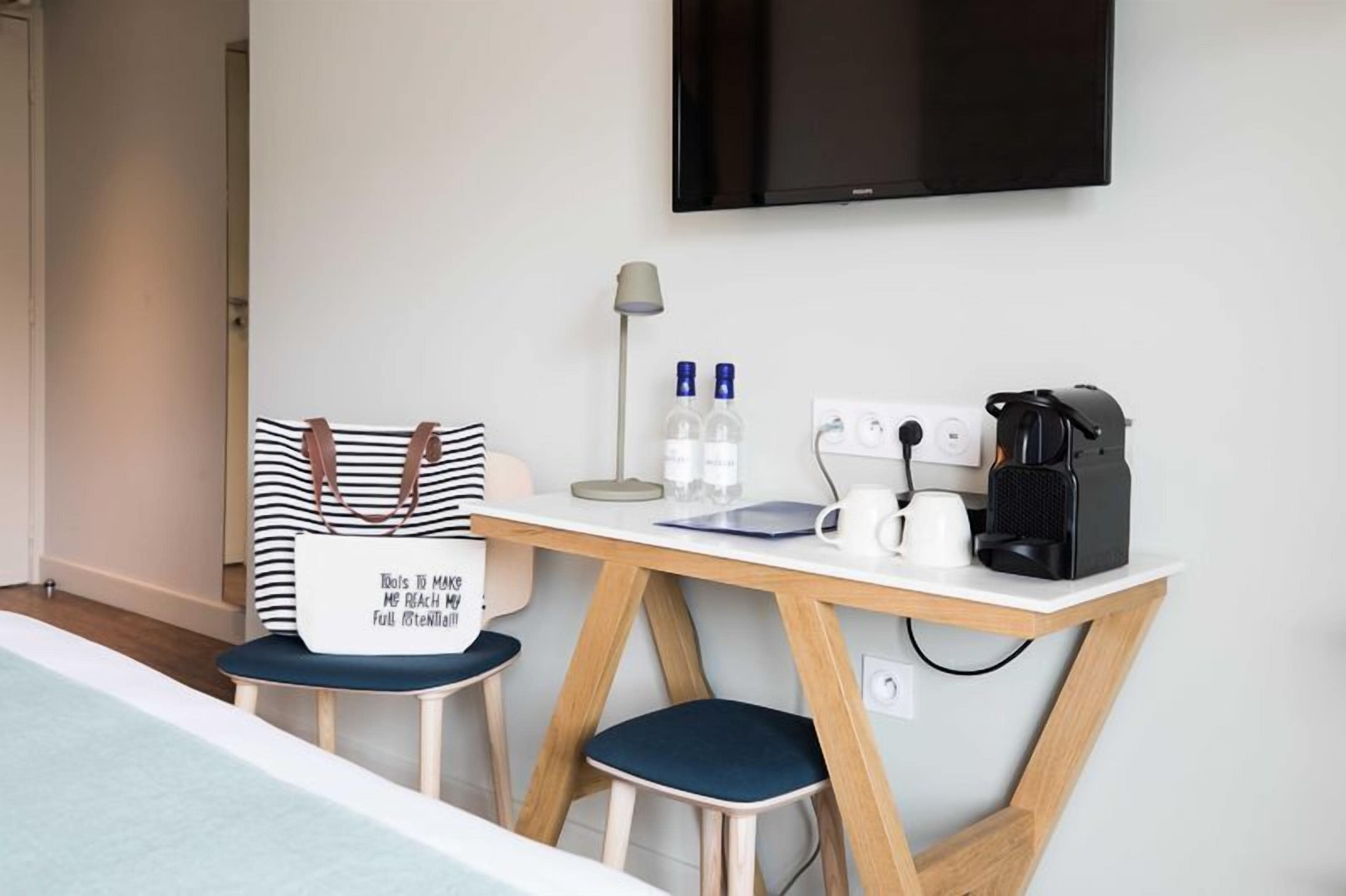 A hotel room with a bed, a desk with a coffee maker, a TV, and a pillow with a motivational quote.