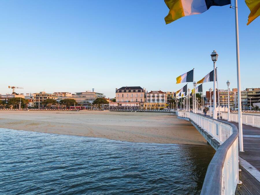 Une promenade en bord de mer avec une passerelle en bois, des drapeaux et des bâtiments en arrière-plan.
