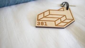 Un llavero de madera con el número 381 sobre una cama con un almohadón azul.