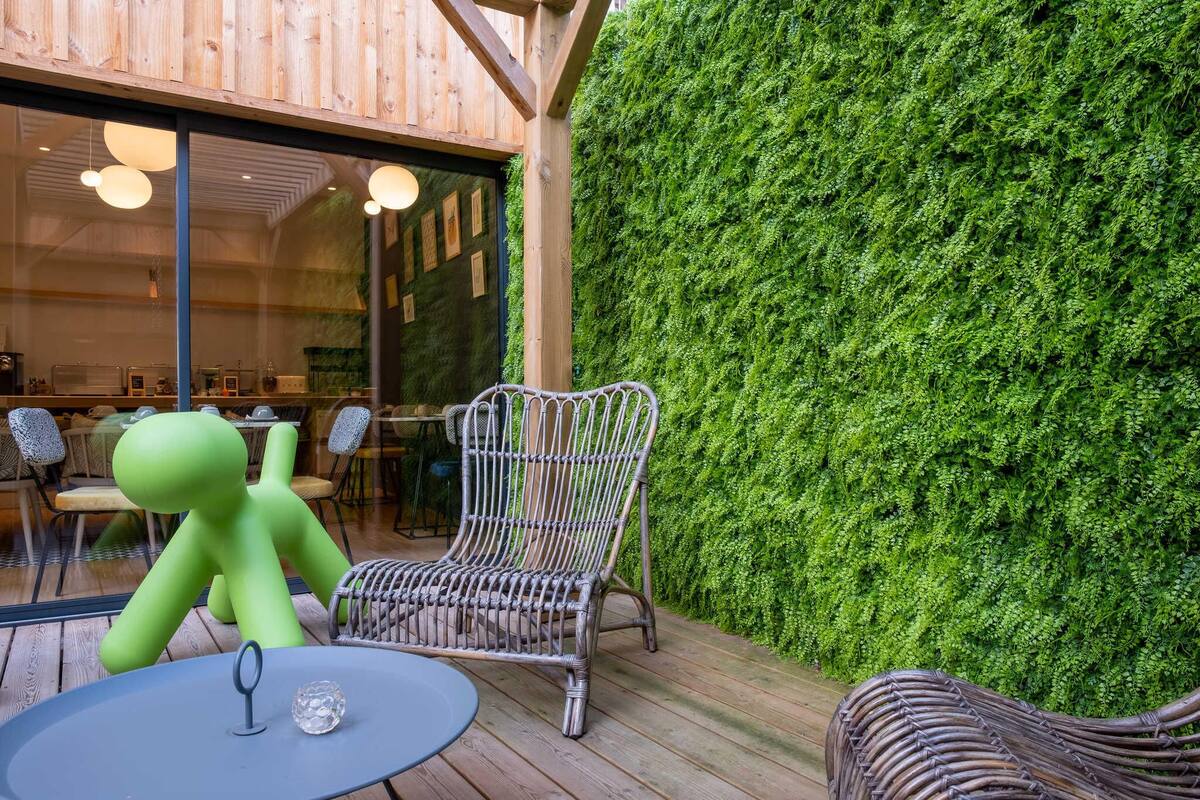 Una terraza de madera con mobiliario de mimbre, una escultura abstracta verde y una pared vertical jardín.