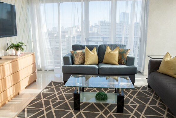 A modern living room with a sofa, a glass coffee table, and a TV on the wall.