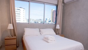 A hotel room with a large bed, two bedside tables, a window with curtains, and a view of buildings.