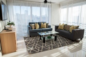 A modern living room with a grey sofa set, a glass coffee table, and a geometric patterned rug.