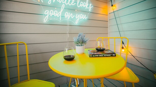 Een gele tafel met een neonbord waarop staat 'Nashville staat je goed', een kamerplant, een wijnglas en een boek getiteld 'Island Fruit Remedy'.