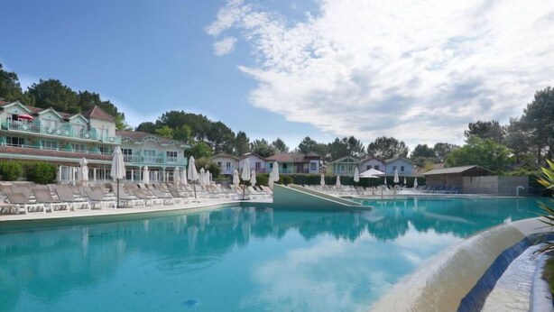 Una piscina con sillones de descanso y sombrillas, rodeada de casas y árboles.