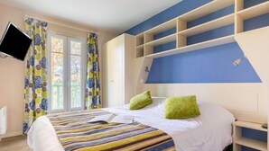 Un dormitorio con cama, televisor montado en la pared y ventana con cortinas.