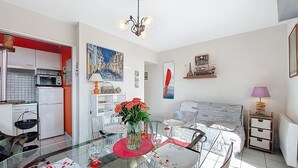 Et moderne køkken med hvide skabe, en mikrobølgeovn og en komfur. Der er et spiseområde med et glasbord, stole og en vase med røde blomster.