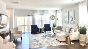 A spacious living room with a large window, a sofa, two armchairs, a coffee table, and a potted plant. - New Modern Home near RDU-1st floor bedroom (Durham)