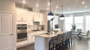A modern kitchen with white cabinetry, stainless steel appliances, and a central island with bar stools. - New Modern Home near RDU-1st floor bedroom (Durham)