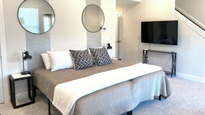 A modern bedroom with a large bed, two bedside tables, a TV, and a staircase. - New Modern Home near RDU-1st floor bedroom (Durham)