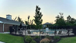 A fenced backyard with a swimming pool, lounge chairs, and a brick building. - New Modern Home near RDU-1st floor bedroom (Durham)