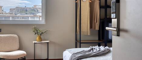 A bedroom with a bed, a chair, a small table with a plant, a wardrobe, and a view of a historic building.