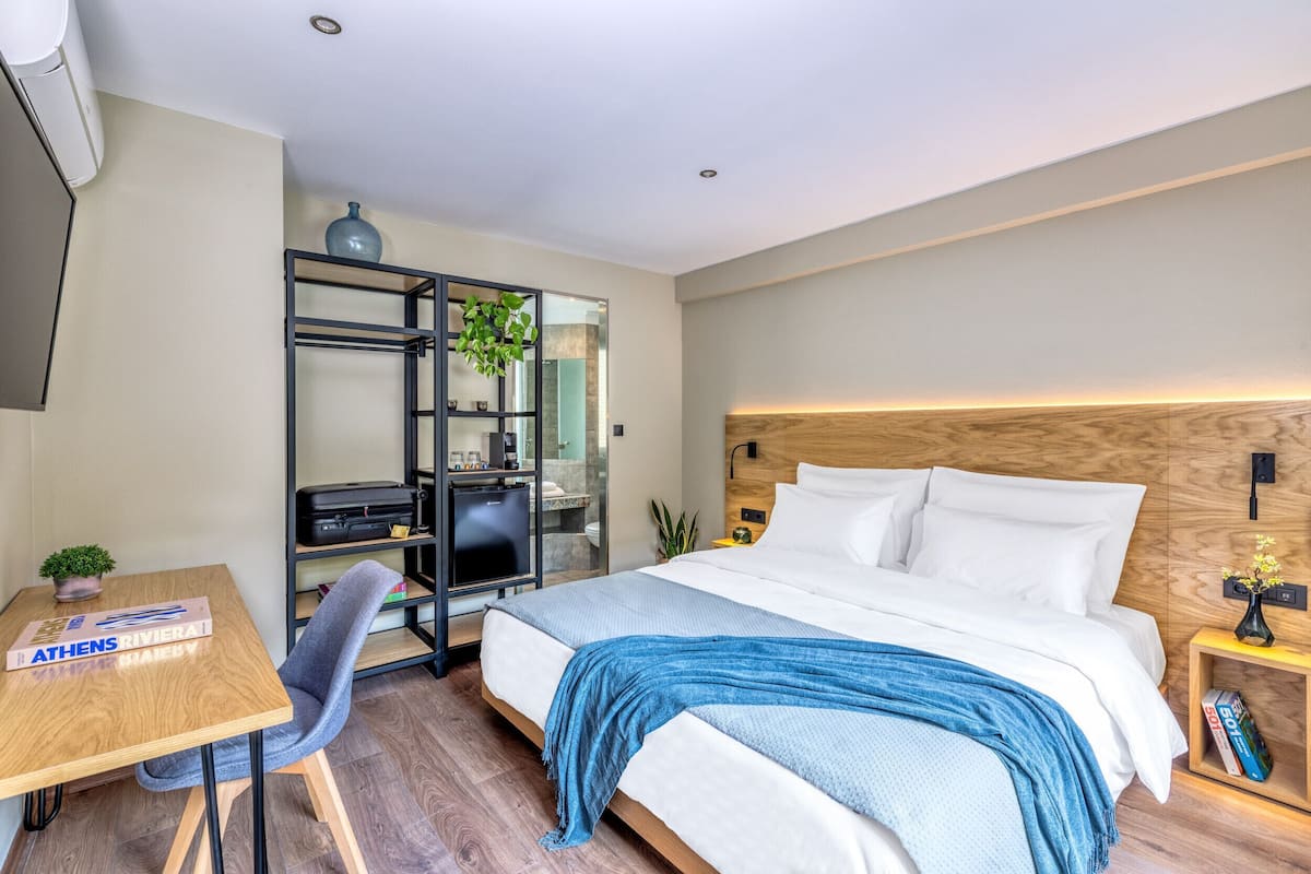 Una habitación de hotel moderna con una cama, un escritorio, una silla, una estantería y una planta pequeña.