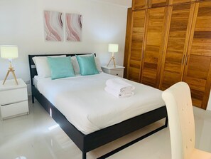 Un letto rifatto con lenzuola bianche e cuscini color acquamarina, un armadio in legno e due comodini con lampade.