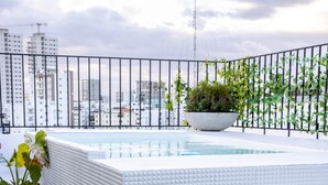 A rooftop pool with tiled steps, surrounded by potted plants and a metal railing.