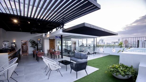 A rooftop terrace with modern furniture, a bar area, and a view of the city skyline.
