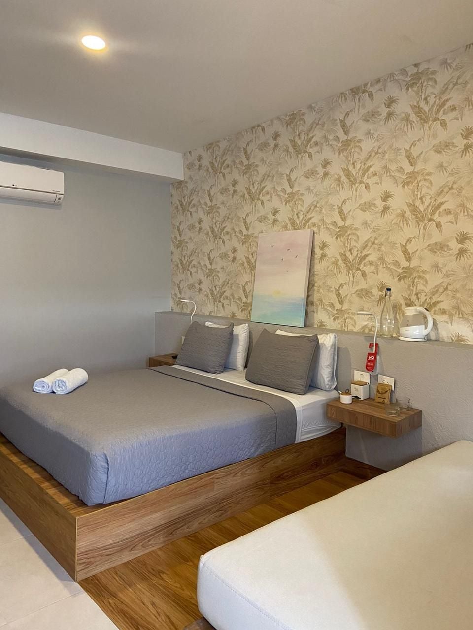 A bedroom with a bed, a bedside table, a wall-mounted air conditioner, and a painting.