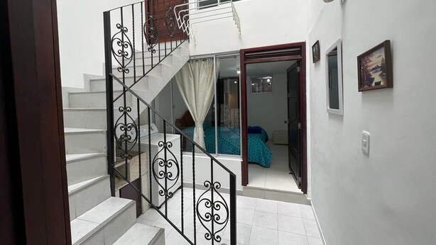 Un escalier orné de rampes noires menant à une chambre à coucher où se trouvent un lit et une fenêtre.