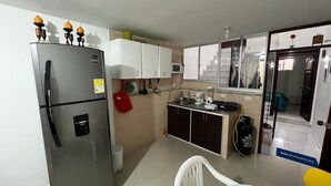 Une cuisine compacte équipée d’un réfrigérateur, de meubles blancs, d’un four à micro-ondes et d’une machine à café.