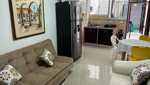 Un salon avec un canapé, une table à manger avec des chaises, un réfrigérateur et un coin cuisine équipé de placards et d’une fenêtre.