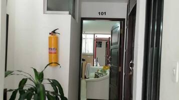 A hallway with a fire extinguisher mounted on the wall, a potted plant, and a door labeled "101".