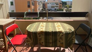Een balkon buiten met een tafel en stoelen, een uitzicht op gebouwen achtergrond, en een gestreepte luifel erboven.